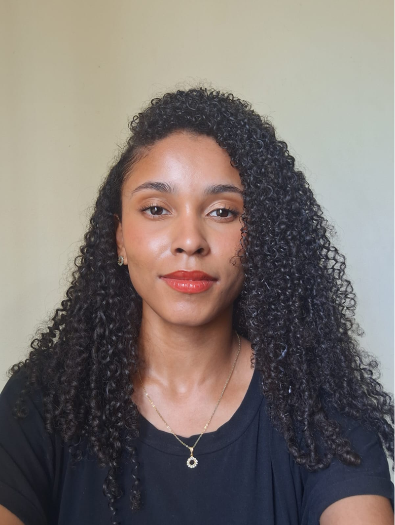 Manuela Valentin: mulher jovem, pele morena clara, cabelo encaracolado comprido.